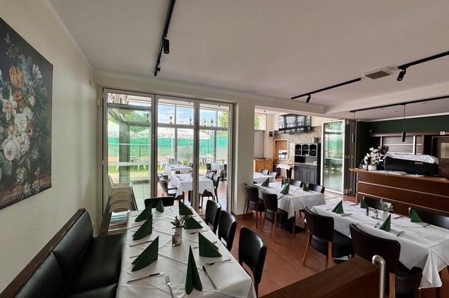 Gem&uuml;tlicher Restaurantbereich mit Tischen, gedeckt mit wei&szlig;en Tischdecken und gr&uuml;nen Servietten, daneben Fenster mit Ausblick.