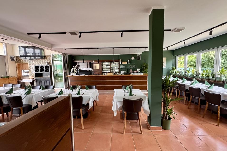 Innenansicht eines Restaurants mit mehreren Tischen, einem Thekenbereich und gro&szlig;en Fenstern.