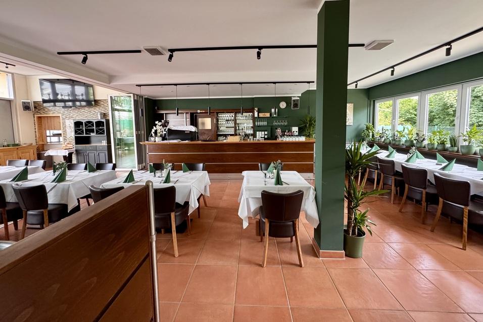 Innenansicht eines Restaurants mit mehreren Tischen, einem Thekenbereich und gro&szlig;en Fenstern.