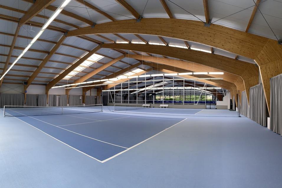 Panoramaansicht einer modernen Tennishalle mit blauen Spielfeldern und Holzdetails im Architekturstil.