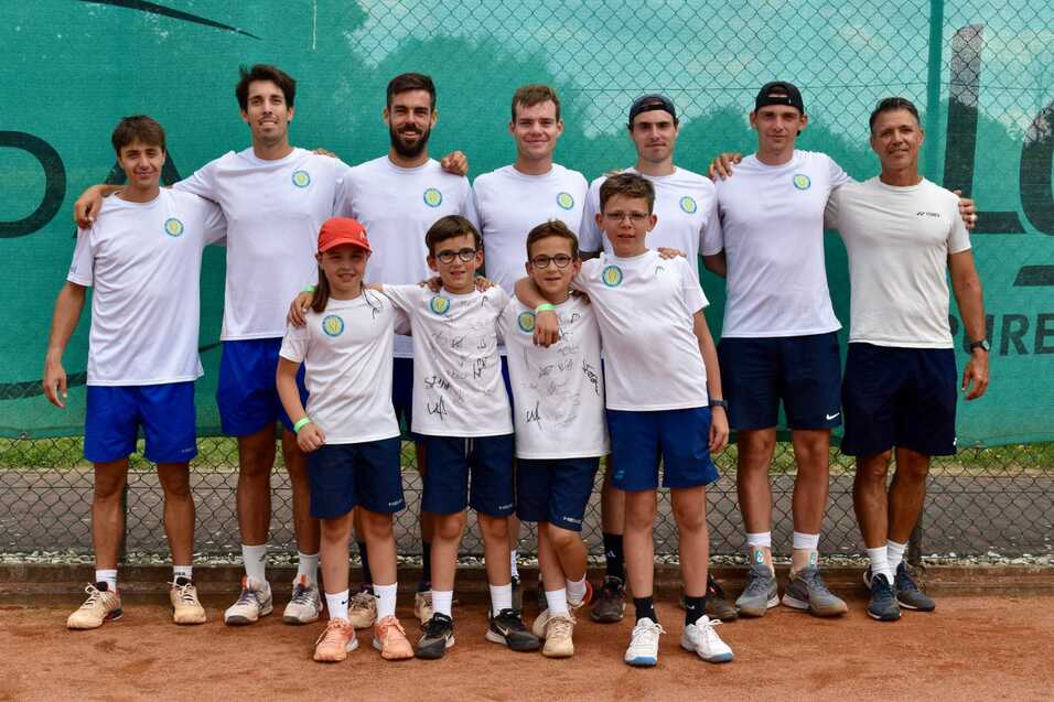 Eine Gruppe von acht Erwachsenen und vier Kindern, alle in sportlicher Kleidung, posiert l&auml;chelnd auf einem Tennisplatz.
