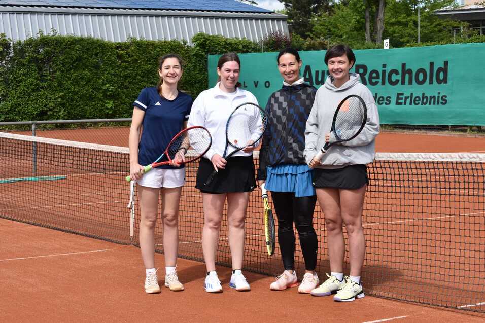 Vier Damen stehen am Tennisnetz auf einem Sandplatz, jede mit einem Tennisschl&auml;ger in der Hand.