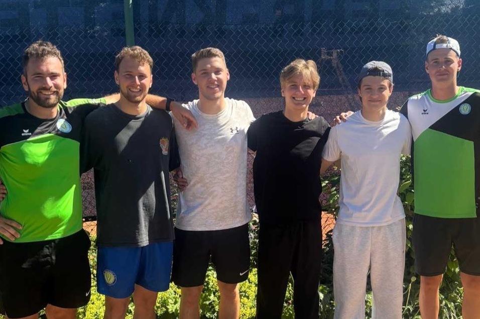 Sechs junge M&auml;nner in sportlicher Kleidung stehen l&auml;chelnd nebeneinander auf einem Tennisplatz.