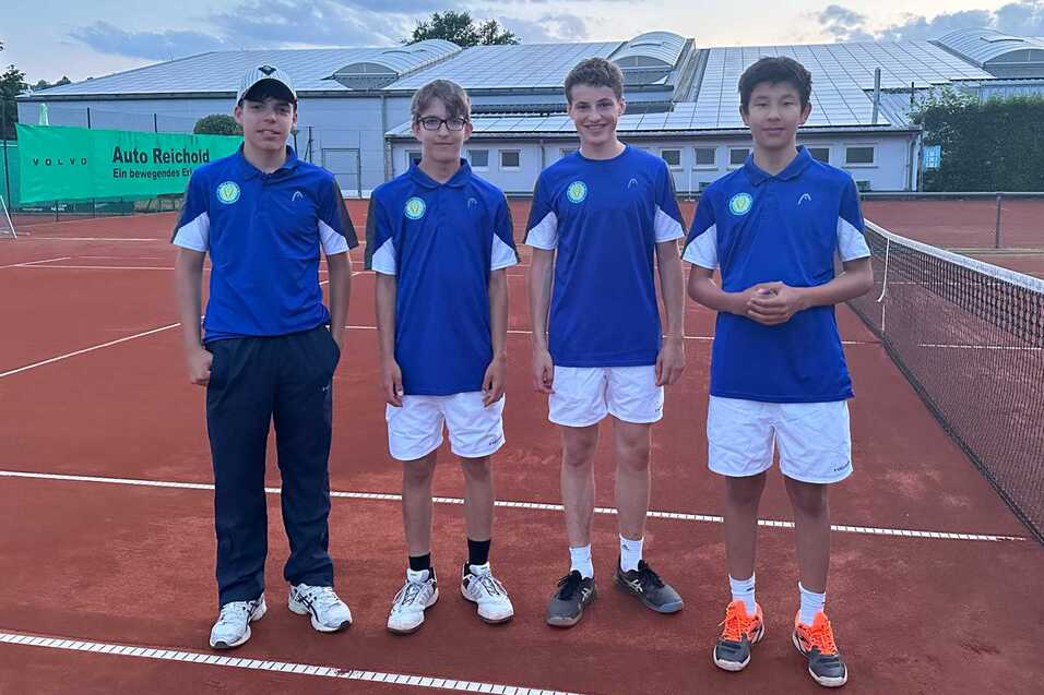 Vier Jugendliche in blauen Tennis-Trikots stehen auf einem roten Tennisplatz, bereit f&uuml;r das Training.