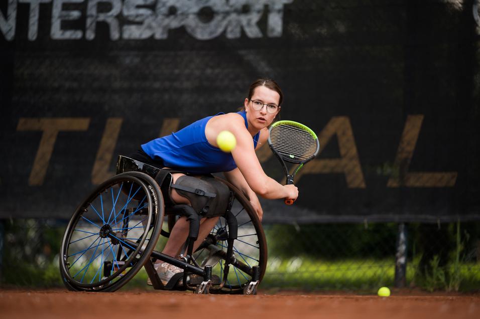 Eine Sportlerin im Rollstuhl spielt Tennis und trifft einen Ball auf einem Tennisplatz.
